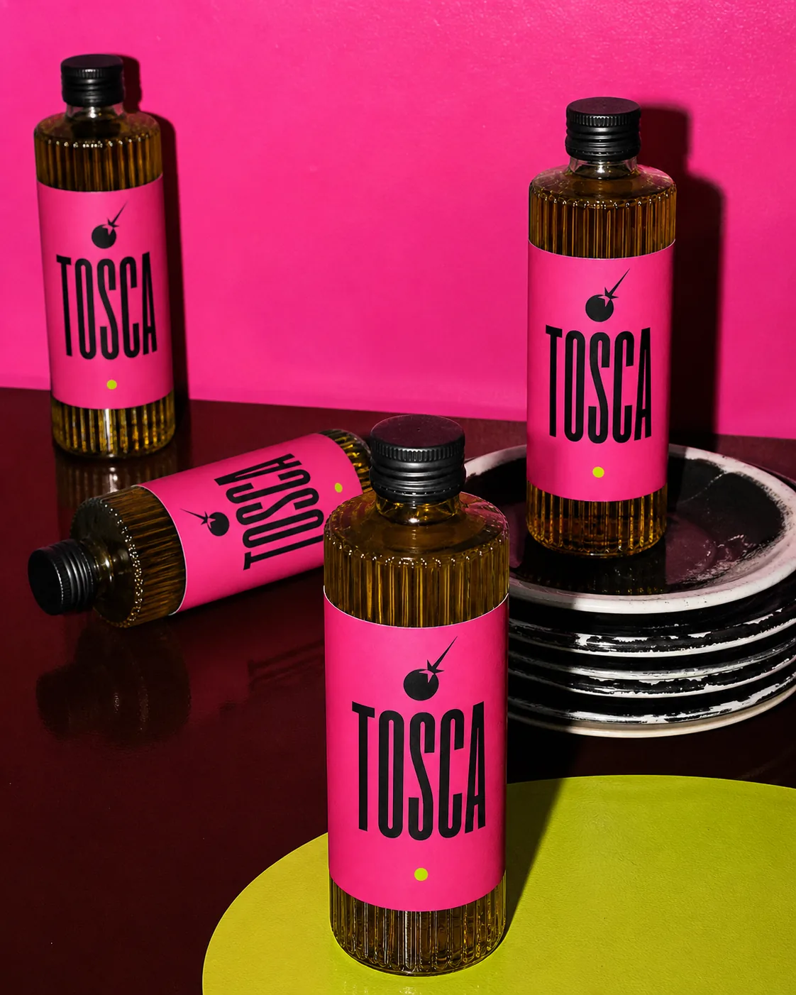 Repetición de botellas TOSCA sobre vajilla negra y fondo fucsia